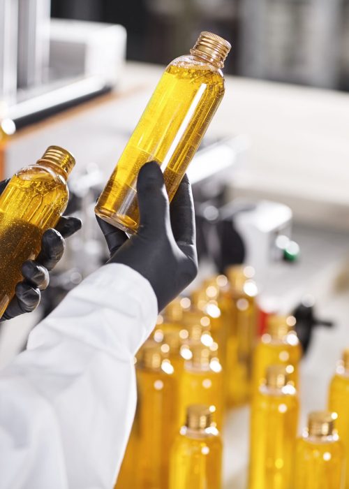 Manufacturing concept. Factory worker holding two glass bottles with yellow liquid comparing quality between them. Factory process of production shampoo. Technology, innovation and scientific concept